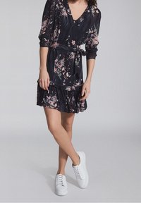 Blommig omlottklänning i mörkblått med rosa och gröna mönster, långa ärmar, V-ringning, lagerkjol, och matchad med vita sneakers.