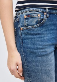 Άτομο που φοράει μπλε τζιν και μπλε ριγωτό πουκάμισο, με το χέρι χαλαρό στο πλάι, κοντινό πλάνο στη μέση και το πάνω μέρος του μηρού.