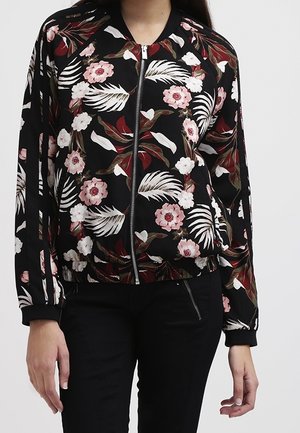 Schwarze Jacke mit Reißverschluss mit rosa-weißen Blumen- und Blättermustern, getragen mit schwarzer Hose.