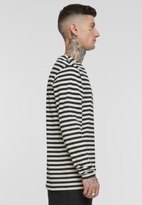 T-shirt à manches longues et col ras du cou avec des rayures horizontales noires et blanches. Fabriqué en tissu à texture douce. Agrémenté de poignets.