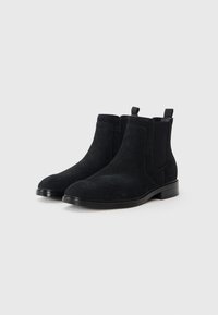 Botas Chelsea de ante negro con paneles laterales elásticos, puntera redondeada, tacón plano y lengüetas para facilitar su puesta. Textura suave y lisa.