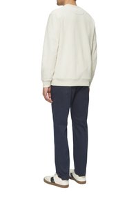 Lichtbeige sweatshirt met ronde hals, ribgebreide boorden en onderkant. Gecombineerd met marineblauwe broek en witte sneakers met zwarte streepaccenten.