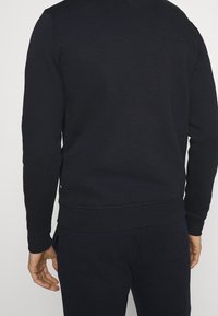 Granatowy sweatshirt wykonany z miękkiego materiału, z okrągłym dekoltem, ściągaczami przy mankietach i u dołu; posiada subtelne detale szwów na dole.