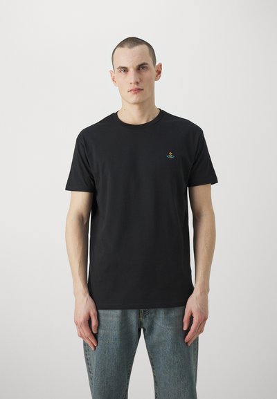 T-shirt noir en coton avec un col rond, des manches courtes et une petite broderie colorée d'une silhouette sur le côté gauche de la poitrine. Coupe décontractée.