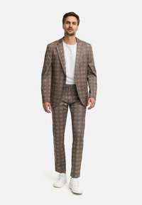 Braun kariertes Anzug mit taillierter Passform, bestehend aus einem einreihigen Blazer und passender Hose, kombiniert mit einem weißen T-Shirt und weißen Sneakers.