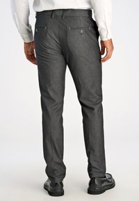 Pantaloni sartoriali grigi con finitura strutturata, dotati di due tasche posteriori con chiusura a bottone. Abbinati a scarpe nere.