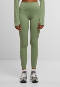 Light green leggings made of stretchy material, featuring a high waistband and a fitted design. Worn with gray athletic shoes and white socks.