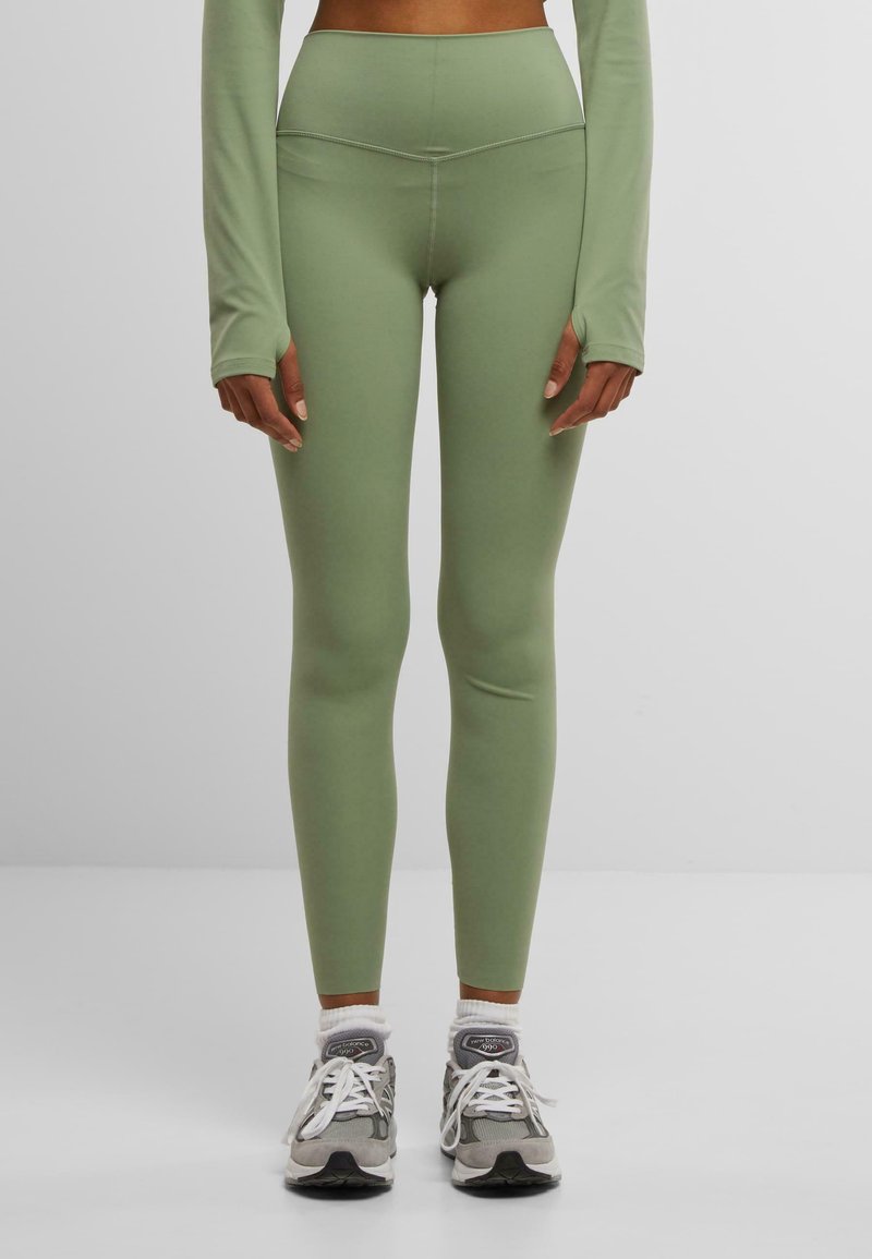 Light green leggings made of stretchy material, featuring a high waistband and a fitted design. Worn with gray athletic shoes and white socks.