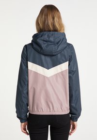 Giacca con cappuccio, caratterizzata da un top blu navy e un design a zig-zag crema e rosa. Realizzata in materiale leggero e resistente all'acqua con polsini elasticizzati.