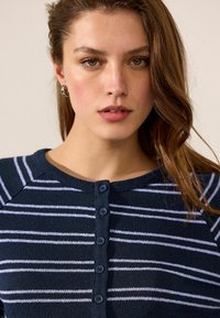 Marineblau gestreifter Cardigan mit Knopfverschluss, der weiße horizontale Streifen, einen Rundhalsausschnitt und eine gerippte Struktur aus weichem Strickstoff aufweist.