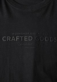 Černá látka s vyraženým textem "Základní vybavení dílny, řemeslné zboží, nepřekonatelný komfort, Street One Muži."