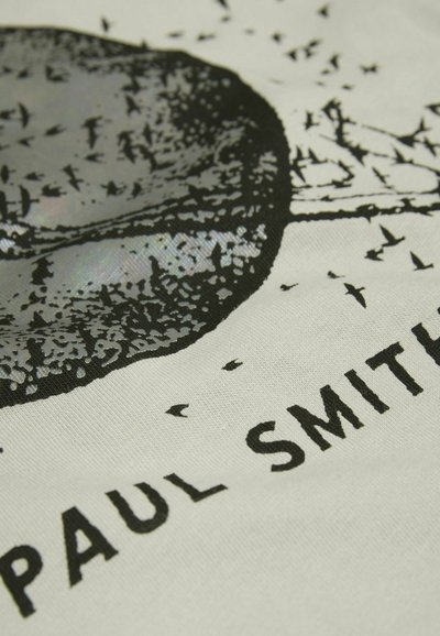 Impresión gráfica en blanco y negro sobre tejido color crema, con un diseño circular que presenta aves y el texto "PAUL SMITH" en letras negritas.