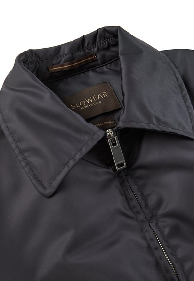 Giacca nera impermeabile con colletto alto, chiusura con zip e superficie liscia, senza texture. Presenta un'etichetta interna con il marchio.