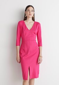 Pink, fitted dress with a V-neck and three-quarter sleeves. Features a central seam and a front slit. Smooth texture and knee-length design.