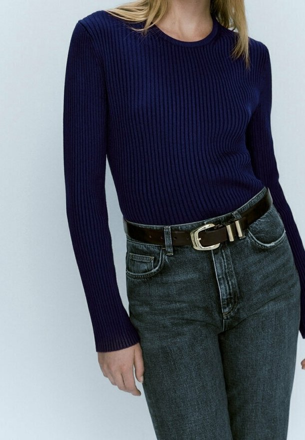 Top a maniche lunghe a coste di colore blu navy abbinato a jeans scuri a vita alta e una cintura marrone con una fibbia metallica.