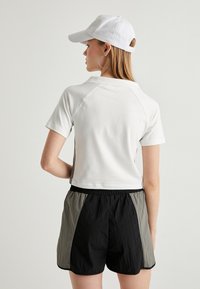 Hvid bomulds T-shirt med korte ærmer, parret med letvægts shorts i sort og grå med elastisk talje og sidelæg. 