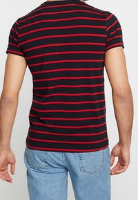 Camiseta de algodón de manga corta a rayas negras y rojas, con cuello redondo y un ajuste entallado, combinada con jeans de color azul claro.