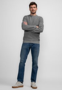 Grauer Strickpullover mit gerippter Textur, Rundhalsausschnitt und langen Ärmeln, kombiniert mit blauen Jeans und hellen Sneakers.