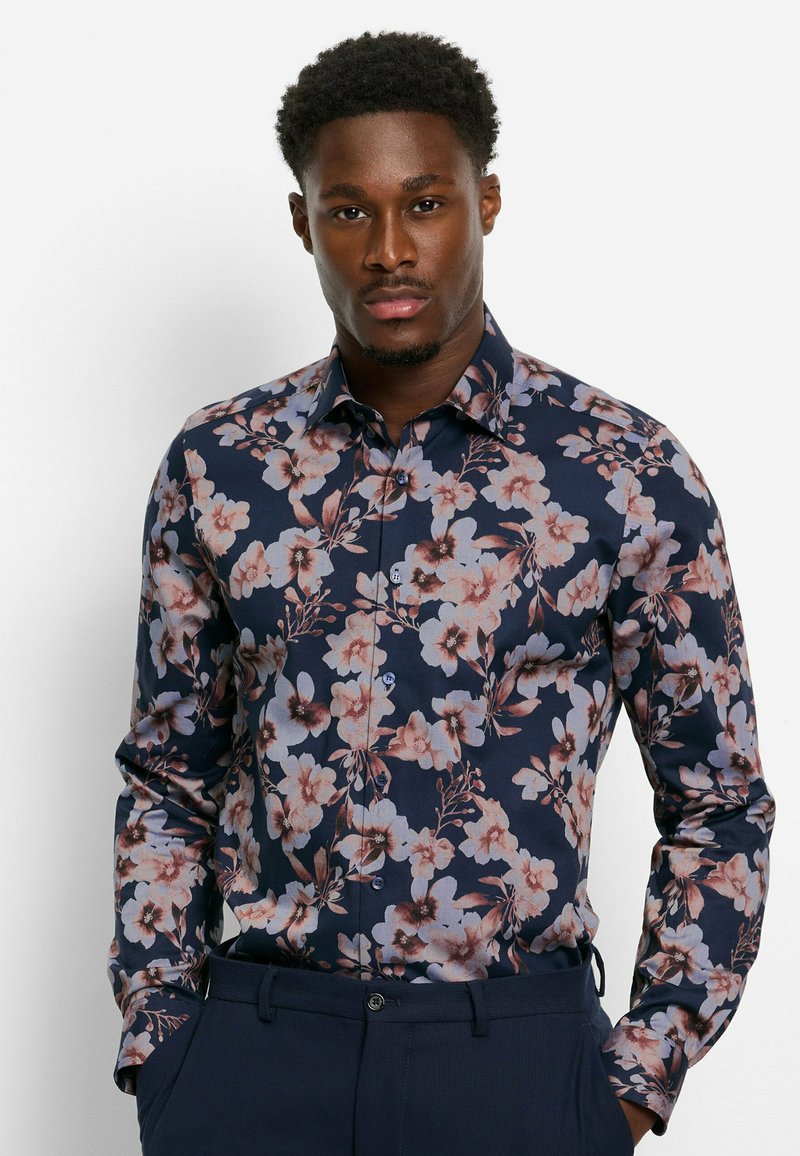 Navy-blaues Blusenshirt mit floralem Muster, das zarte rosa und weiße Blumen mit grünen Akzenten zeigt; lange Ärmel und figurbetonter Schnitt. Glattes Baumwollmaterial.