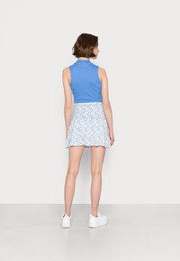 Top azul sem mangas combinado com uma mini saia branca com flores. A saia apresenta um design evasê e uma bainha com babados. Ténis brancos desportivos.