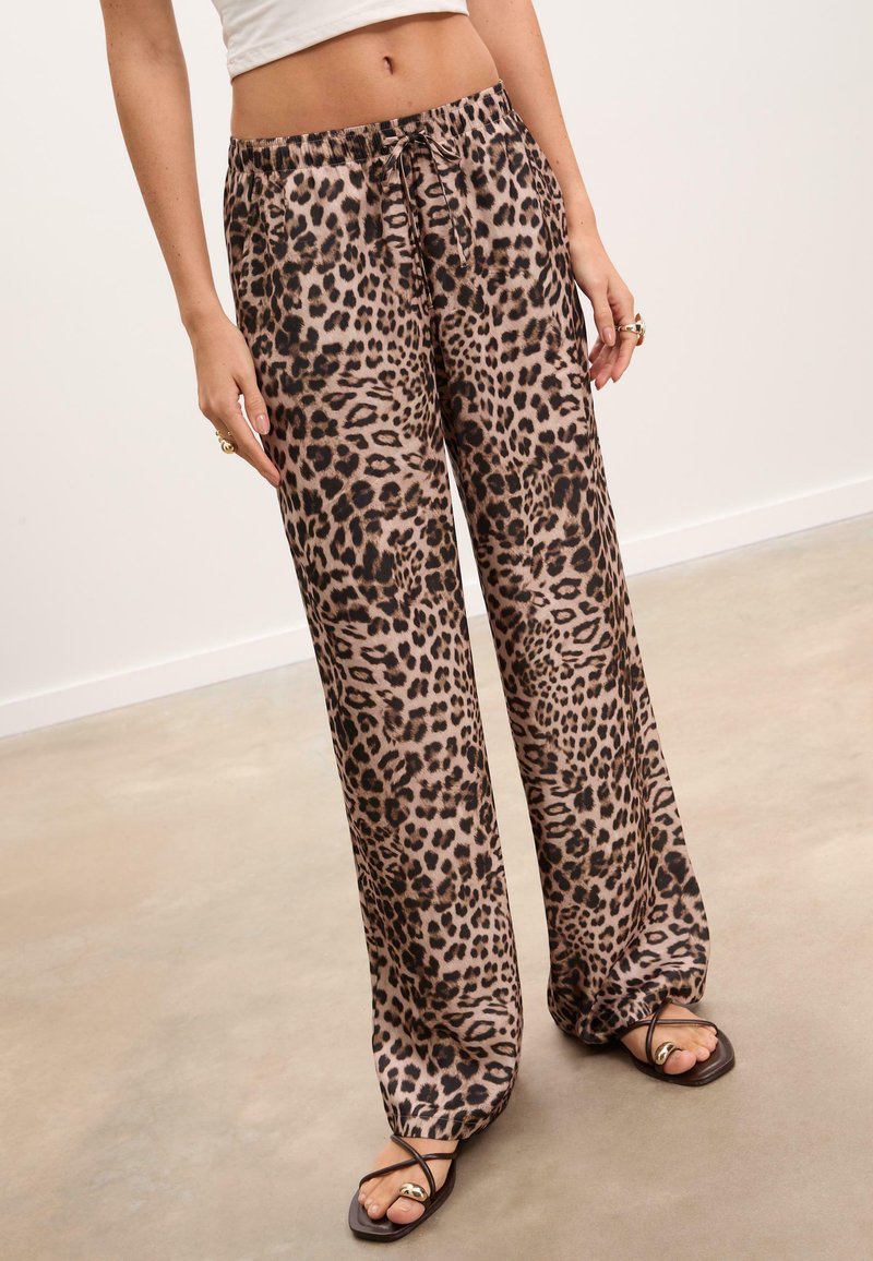 Kalhoty s leopardím potiskem, široké nohavice vyrobené z lehkého materiálu, s elastickým pasem a stahovací šňůrkou. Stylizováno s černými sandály.