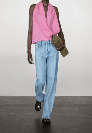 Modelka nosząca różowy, bezrękawnikowy top z drapowaniem, jasnoniebieskie, wysokie jeansy i czarne sandały z odkrytymi palcami, trzyma brązową kopertówkę.