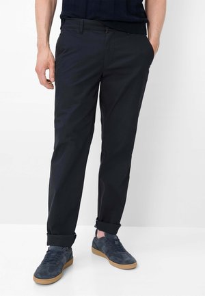 Uomo che indossa pantaloni neri slim-fit risvoltati alle caviglie abbinati a sneakers in suede blu scuro con suole in gomma.
