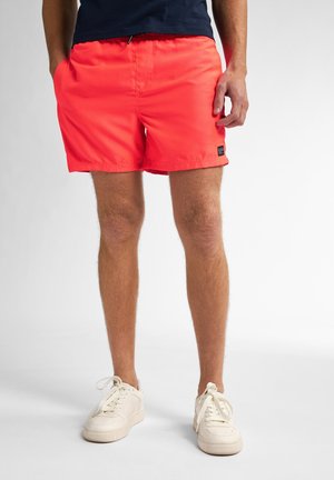 Bañador naranja coral brillante con una cinturilla elástica, bolsillos laterales y un pequeño parche de logo de la marca en la pierna izquierda. Tejido ligero texturizado.