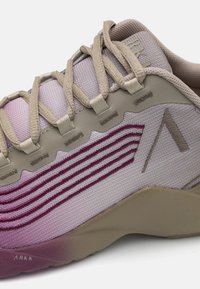 Beżowe buty sportowe z teksturowaną cholewką, z gradientem od jasnofioletowego do bordowego oraz wyraźnymi rowkami w bocznym wzornictwie.