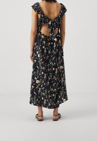 Svart blommig maxiklänning med volangärmar, knytning i ryggen och en lös passform. Har orangea och gröna blommönster mot en mörk bakgrund.