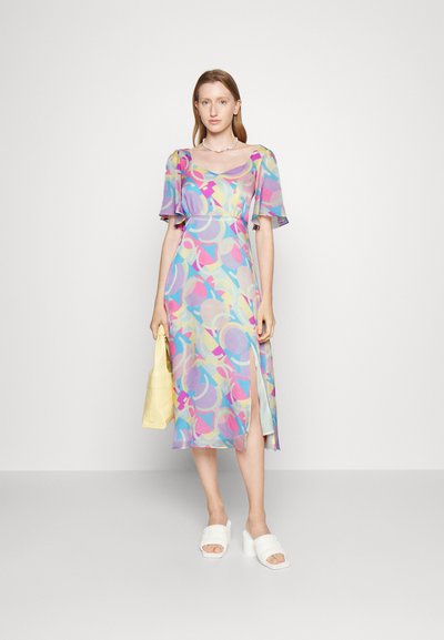Vestido midi com padrão floral em cores pastel, com mangas curtas, uma fenda lateral e um tecido suave e leve. Acompanhado de sandálias brancas e uma bolsa amarela.