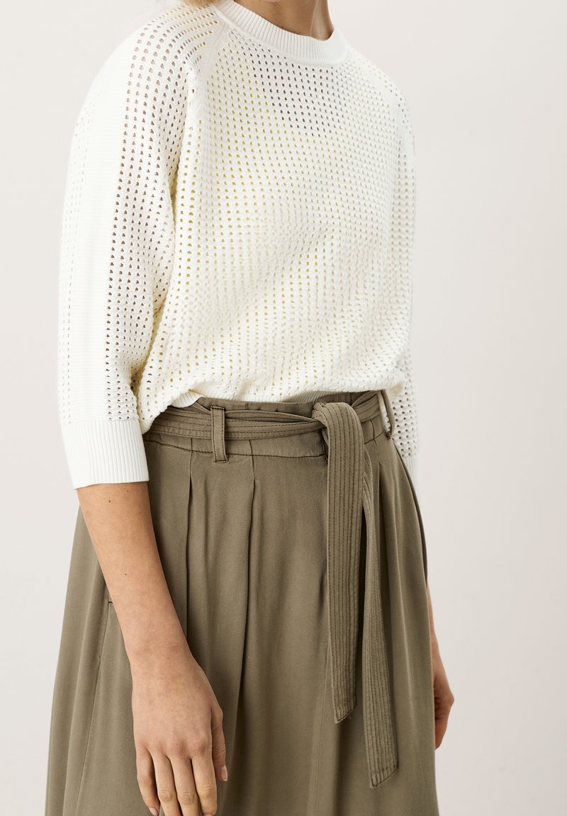 Biały dziany sweter z otwartym wzorem tkania i ściągaczami na rękawach, zestawiony z oliwkowozielonymi, plisowanymi spodniami o wysokim stanie oraz materiałowym paskiem.