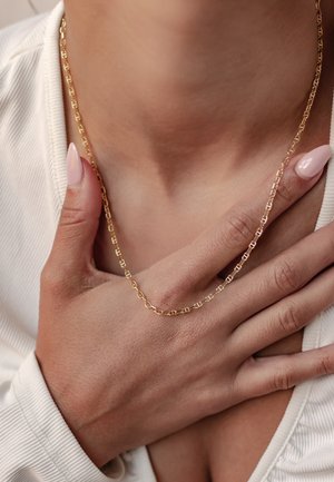Gold chain necklace displayed against skin, featuring circular link design. A hand lightly holds the necklace, with light reflection on the gold.