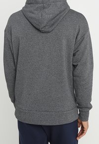 Grå huvtröja med dragsko, raglanärmar och ribbad fåll. Mjuk textur, minimala sömnadsdetaljer på baksidan.