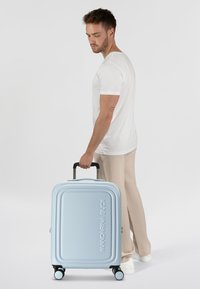 Valigia rigida blu chiaro con design rigato, maniglia per il trasporto e quattro ruote girevoli. Logo "Mandarina Duck" in evidenza.
