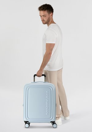 Hellblauer Hartschalenkoffer mit geripptem Design, Tragegriff und vier Spinner-Rädern. Das Logo "Mandarina Duck" ist prominent platziert.