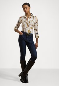 Camicia bianca con design stampato colorato, jeans in denim blu scuro e stivali neri in pelle alti fino al ginocchio con tacco grosso. Accenti dorati sulla cintura.