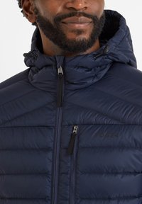 Navy padded jacket with a high collar and attached hood. Features horizontal stitching, two zippered pockets, and a logo on the chest.