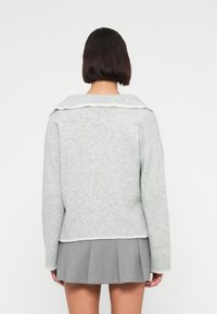 Ανοιχτό γκρι πλεκτό πουλόβερ με φαρδιά γιακά, ριμπ μανσέτες και τελείωμα. Διαθέτει απαλή υφή και άνετη εφαρμογή. Συνδυάζεται με γκρι πλισέ φούστα από κάτω.