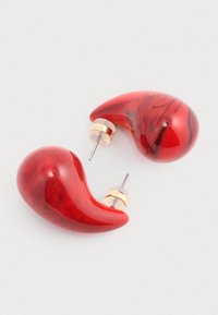 Czerwone kolczyki z żywicy w zakrzywionym, kroplowym kształcie z błyszczącym wykończeniem. Akcenty w kolorze złota na podstawie sztyftów.