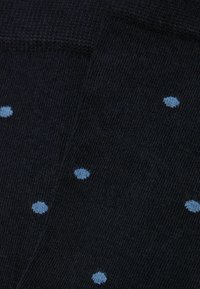 Calcetines de tela negra con un acabado texturizado, que presentan lunares azules distribuidos uniformemente por toda la superficie.