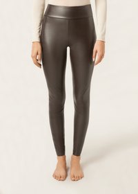 Svarta leggings i faux läder med hög midja, slät textur och en tight passform som sträcker sig ner till anklarna, bärs barfota.