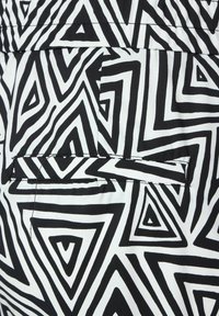 Un tissu à motif noir et blanc avec de grands triangles géométriques. Surface texturée avec une poche, couture visible le long des bords.