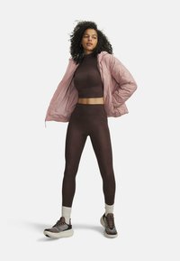 Brown cropped top and high-waisted leggings made of textured fabric, layered with a light pink puffy jacket. Grey sneakers with black accents.
