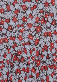 Tissu floral présentant des fleurs rouges et bleu clair sur un fond sombre, avec des détails plissés le long du bord inférieur.