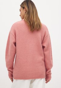 Suéter rosa de gran tamaño con un acabado suave y texturizado, hombros caídos y puños y dobladillo acanalados. Diseño ligero y casual.