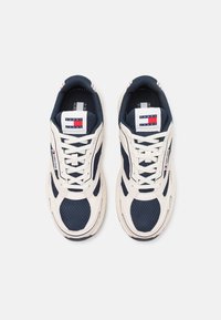 Baskets en filet navy et synthétiques beige, avec des lacets blancs, un branding rouge et bleu sur la languette et le côté, et une semelle rembourrée.
