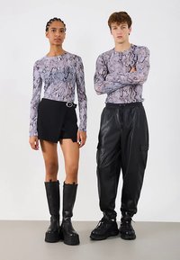 Bluzki z długim rękawem w motyw węża w kolorze fioletowym i szarym, noszone z czarną mini spódniczką z okrągłą klamrą i dopasowanymi czarnymi skórzanymi spodniami.