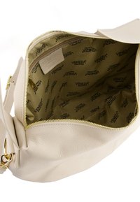 Innenansicht einer cremefarbenen Ledertasche, die eine Reißverschlusstasche zeigt, die mit beigem Stoff gefüttert ist und das wiederholte Branding "VENEZIA" aufweist.