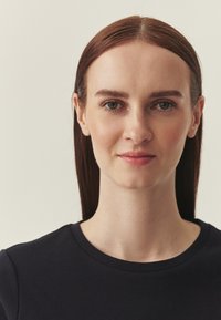 Haut bleu foncé à col ras du cou avec manches courtes, texture lisse, porté par un modèle aux cheveux droits et foncés et maquillage naturel sur un fond clair.